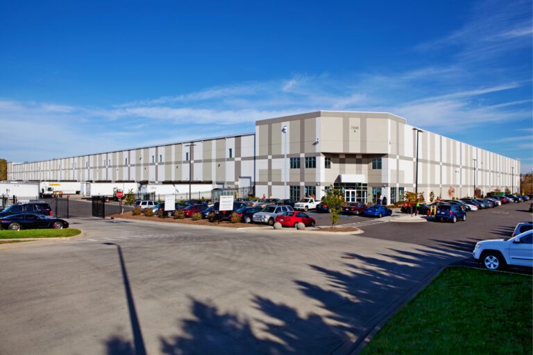 A large industrial warehouse with parking in front under a blue sky.