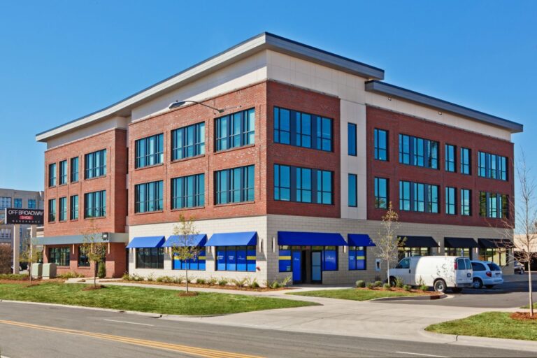 A modern three-story brick office building with large windows and blue awnings.