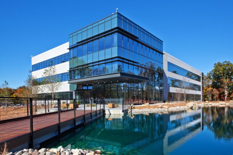 Modern glass office building with a pond in front.