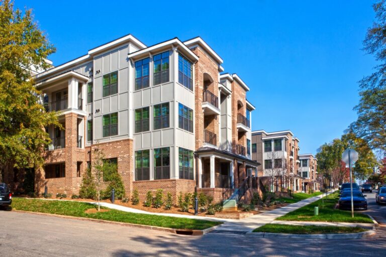 A modern apartment building with brick and siding facade along a tree-lined street.